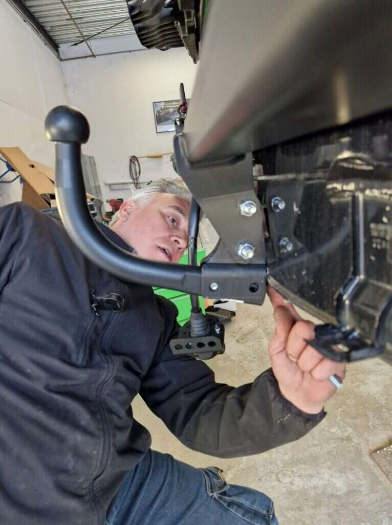 Man monteert een trekhaak onder een voertuig in een werkplaats