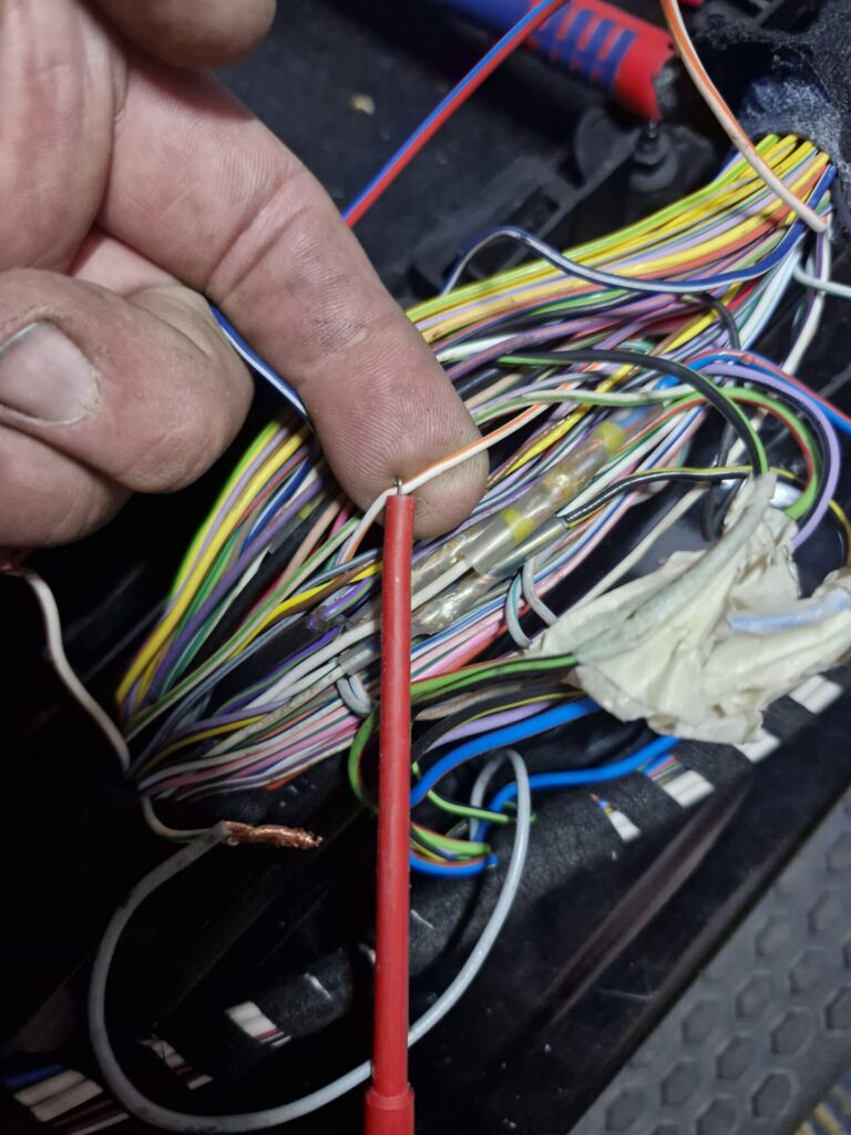 Hand houdt een dunne draad bij een bundel kleurrijke elektrische kabels en een rode meetpen