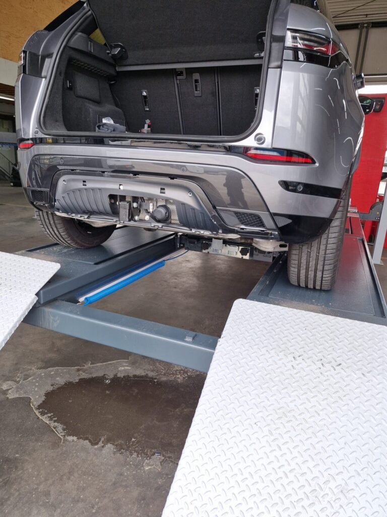 Grijze SUV op hefbrug in werkplaats met geopende achterklep en zichtbare trekhaakmontage