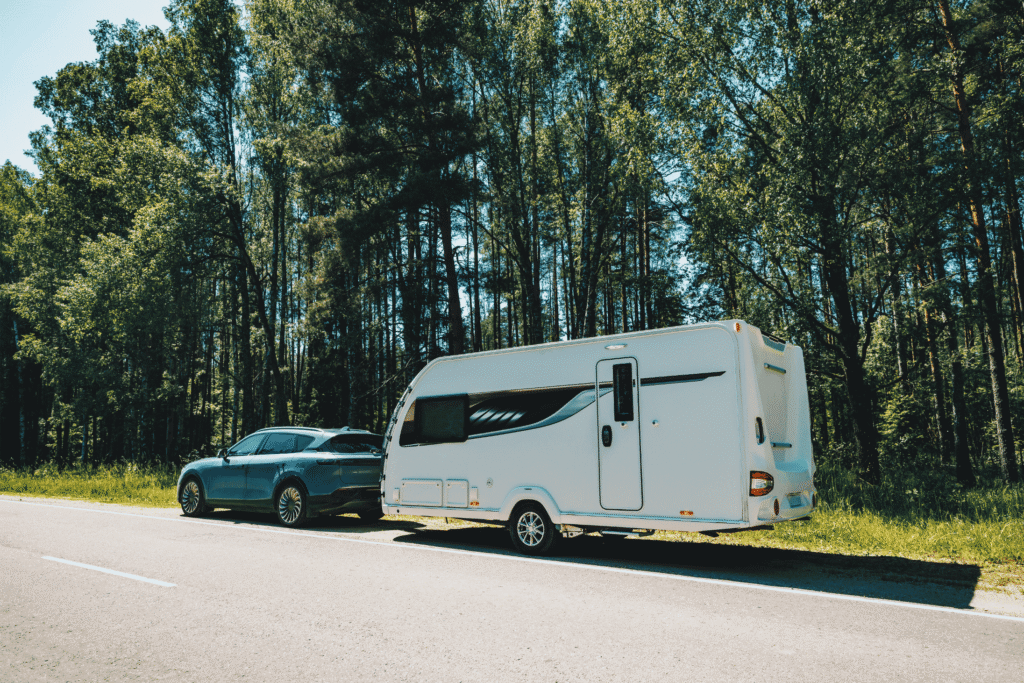Blauwe auto met witte caravan langs een bosrijke weg