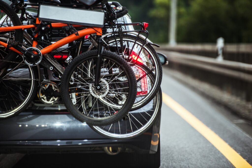 Fietsen achterop een auto op een weg, met een oranje fiets en brandend achterlicht
