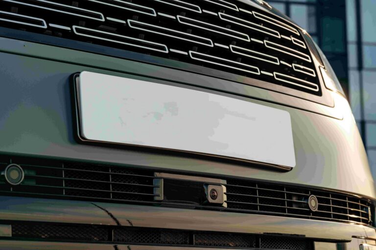 Close-up van de voorkant van een auto met grille, kentekenplaat en camera in de bumper