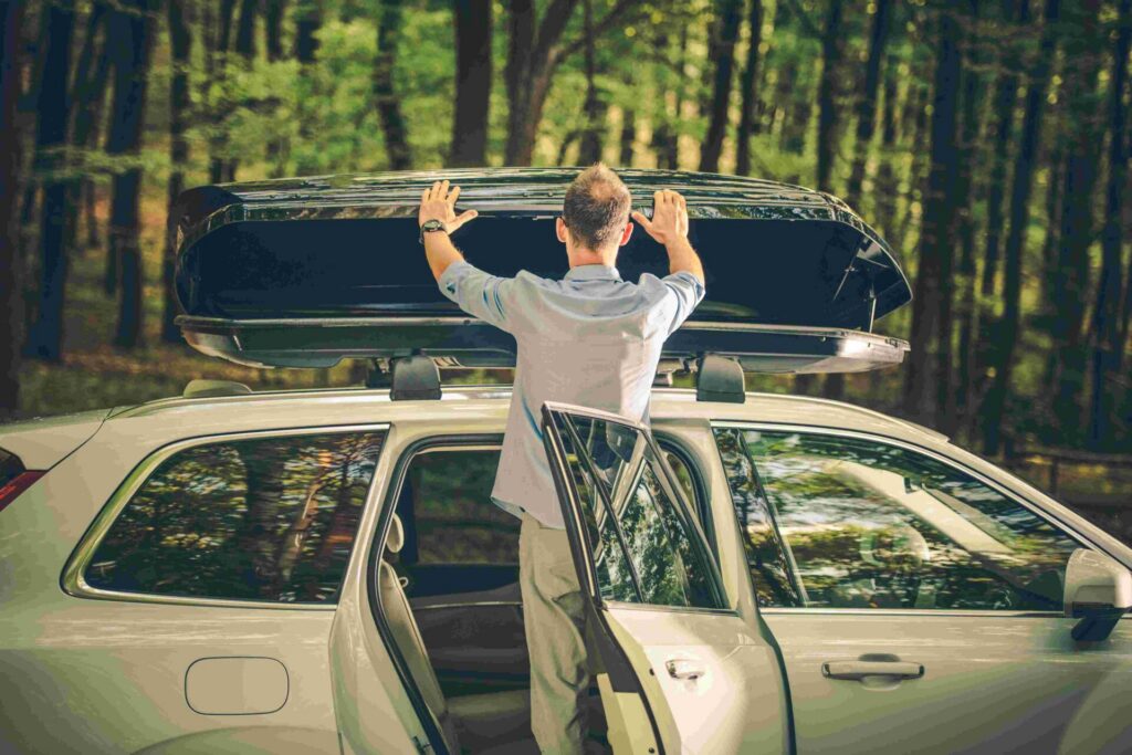 Man opent een dakkoffer op een witte auto in een bos