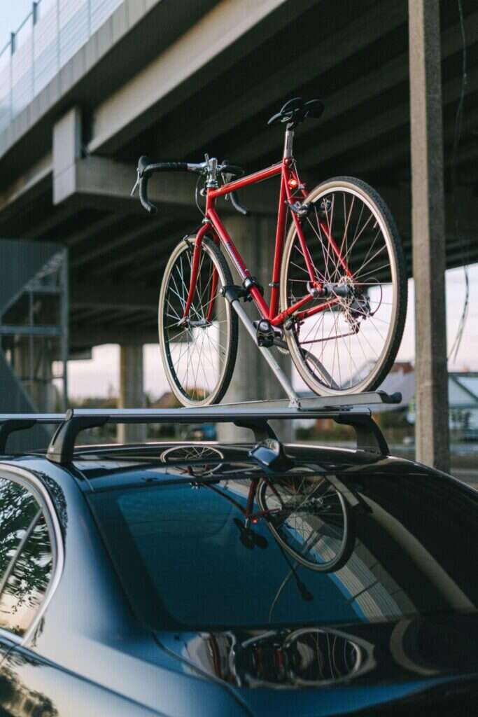 Rode racefiets op een dakdrager van een donkere auto onder een viaduct
