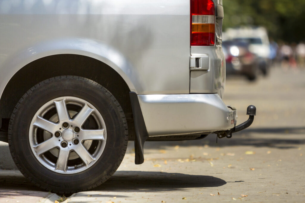 Achterzijde van een zilveren bestelauto met wiel, achterlicht en trekhaak op straat
